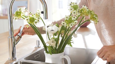A woman fills water into a white vase with white flowers