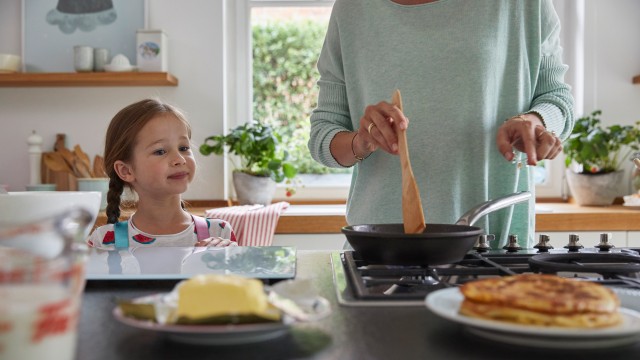 A young girl makes pancakes with her mother