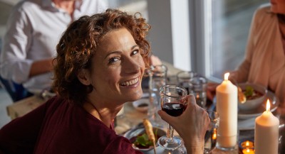 A woman looks happily into the camera and holds a wine glass in her hand
